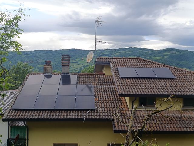 Moduli fotovoltaici neri su due tetti di una casa in collina