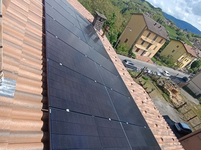 Moduli fotovoltaici neri lungo tutta la falda di un tetto in coppi, sopra il paese